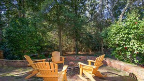 A patio with four wooden Adirondack chairs arranged around a fire pit.