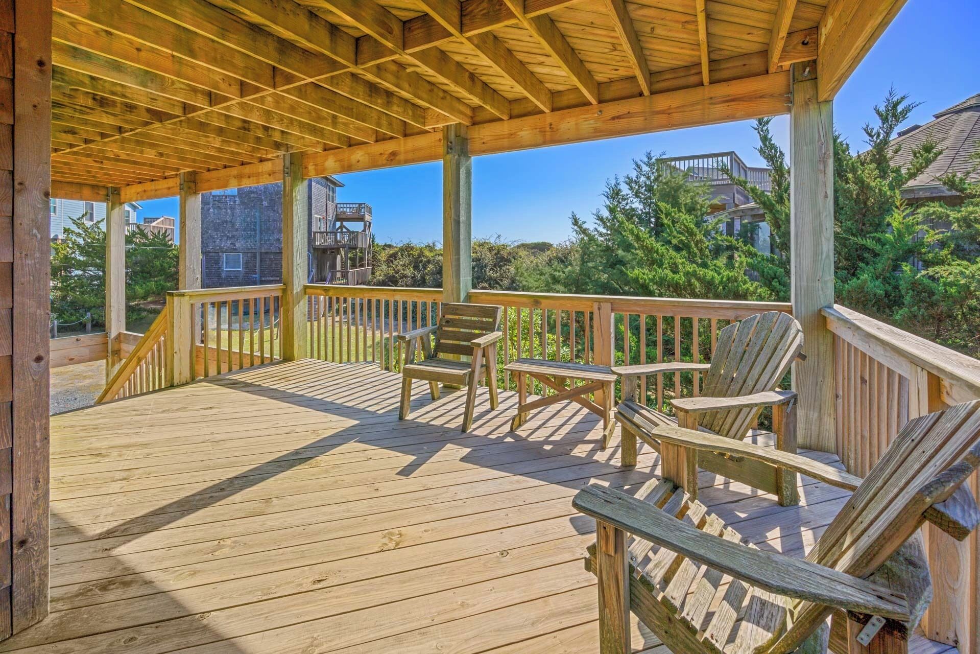 Terraza de madera con sillas Adirondack, barandilla de madera y vista a una zona residencial.