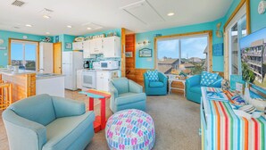 A bright, airy room with teal walls, a kitchenette, and a large window offering a view of the beach. - Fantastic Views! Semi-Oceanfront in Avon, Hot-Tub, Dog-Friendly, Walk to Beach (Avon)