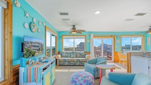 A bright room with a large window, a ceiling fan, and a colorful sofa. - Fantastic Views! Semi-Oceanfront in Avon, Hot-Tub, Dog-Friendly, Walk to Beach (Avon)