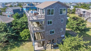 A multi-story wooden building with a balcony on the upper floor, surrounded by trees and other houses. - Fantastic Views! Semi-Oceanfront in Avon, Hot-Tub, Dog-Friendly, Walk to Beach (Avon)