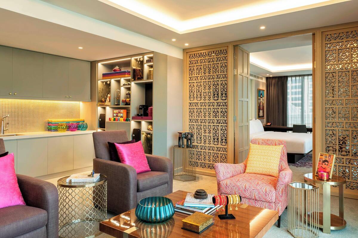 A modern hotel room with grey and pink armchairs, a wooden coffee table, and a decorative partition with intricate patterns.