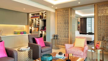 Une chambre d’hôtel moderne avec des fauteuils gris et roses, une table basse en bois et un paravent décoratif aux motifs complexes.