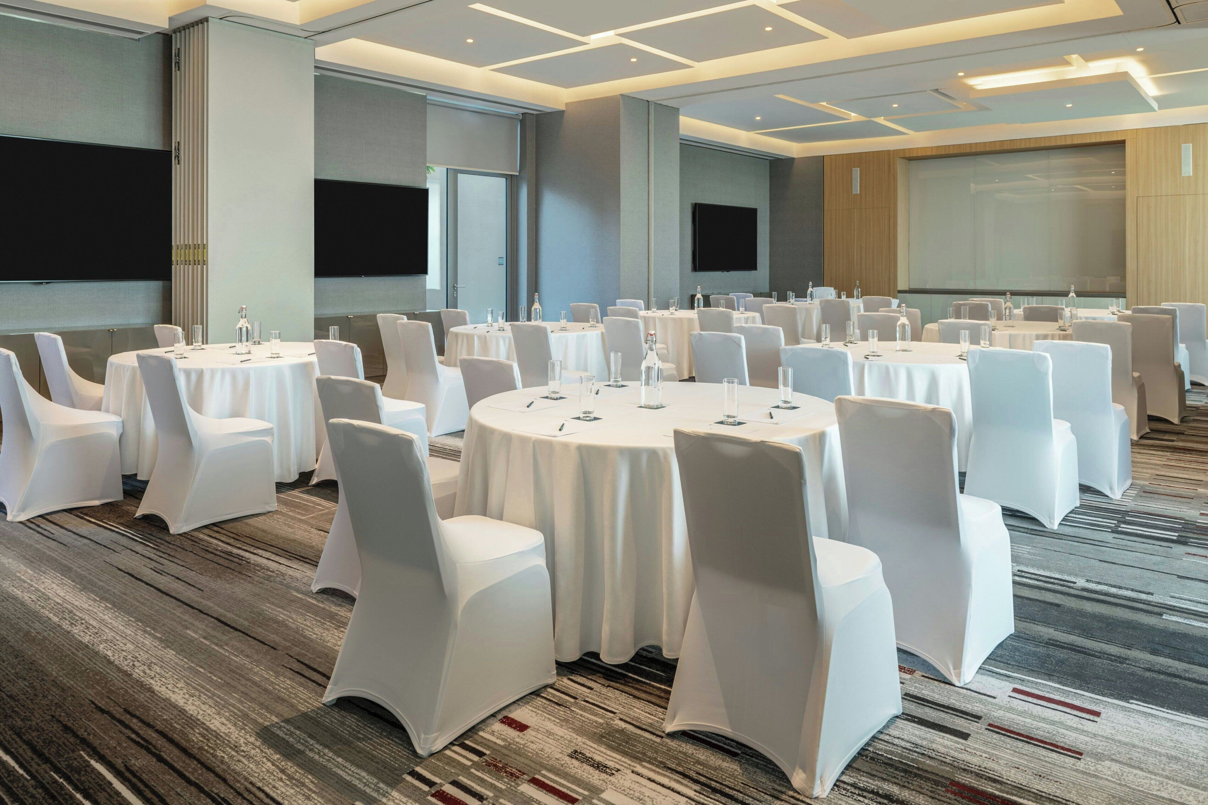 A conference room with multiple round tables, white chairs, and a carpeted floor.