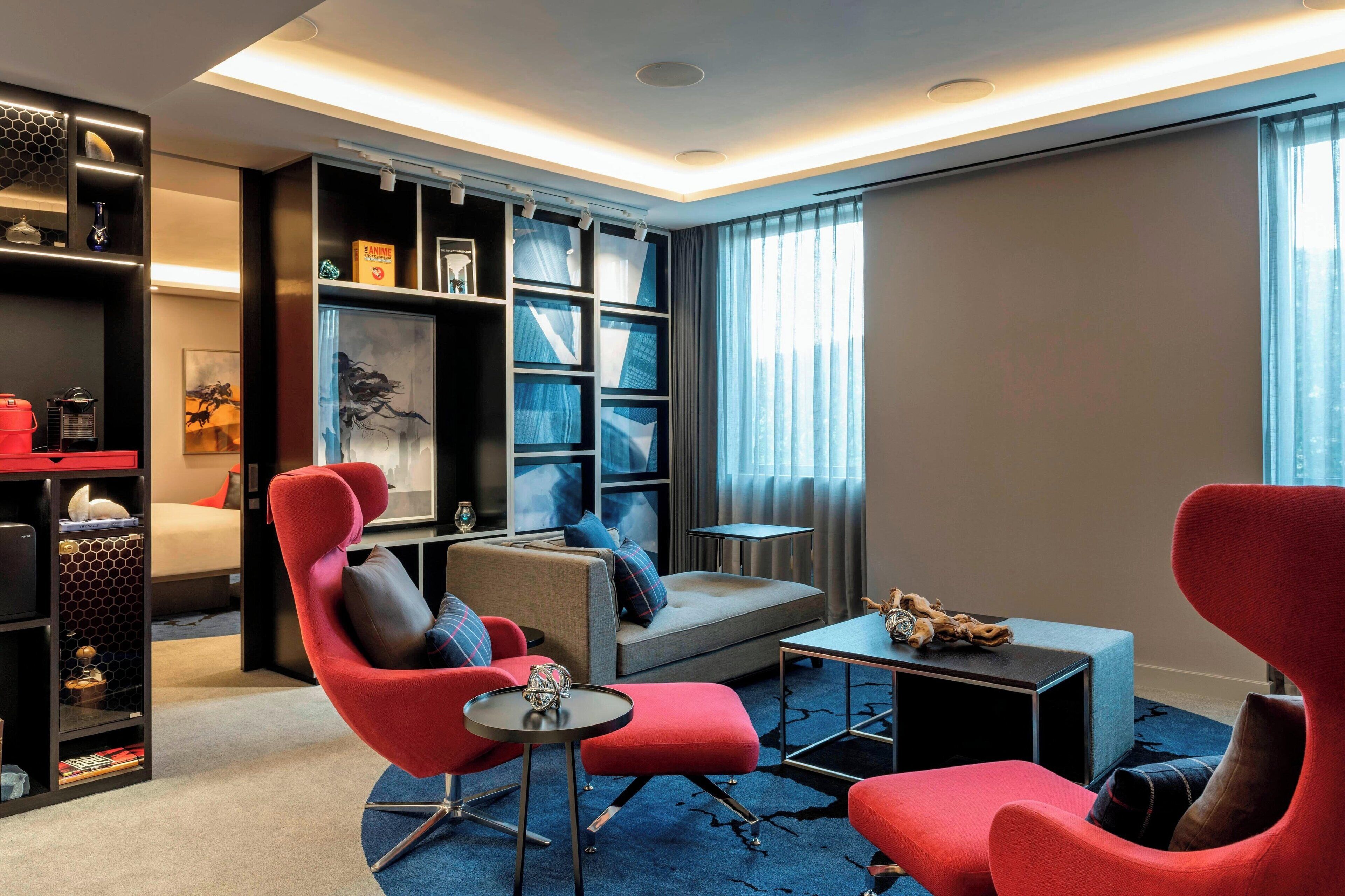 Una sala de estar moderna con un sofá, sillones rojos, una mesita de centro y una estantería.