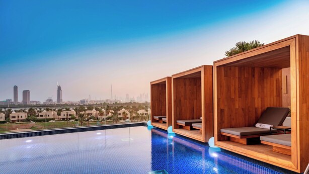 A rooftop infinity pool with wooden loungers and a cityscape view. - Aloft by Marriott Dubai Creek (Dubai)