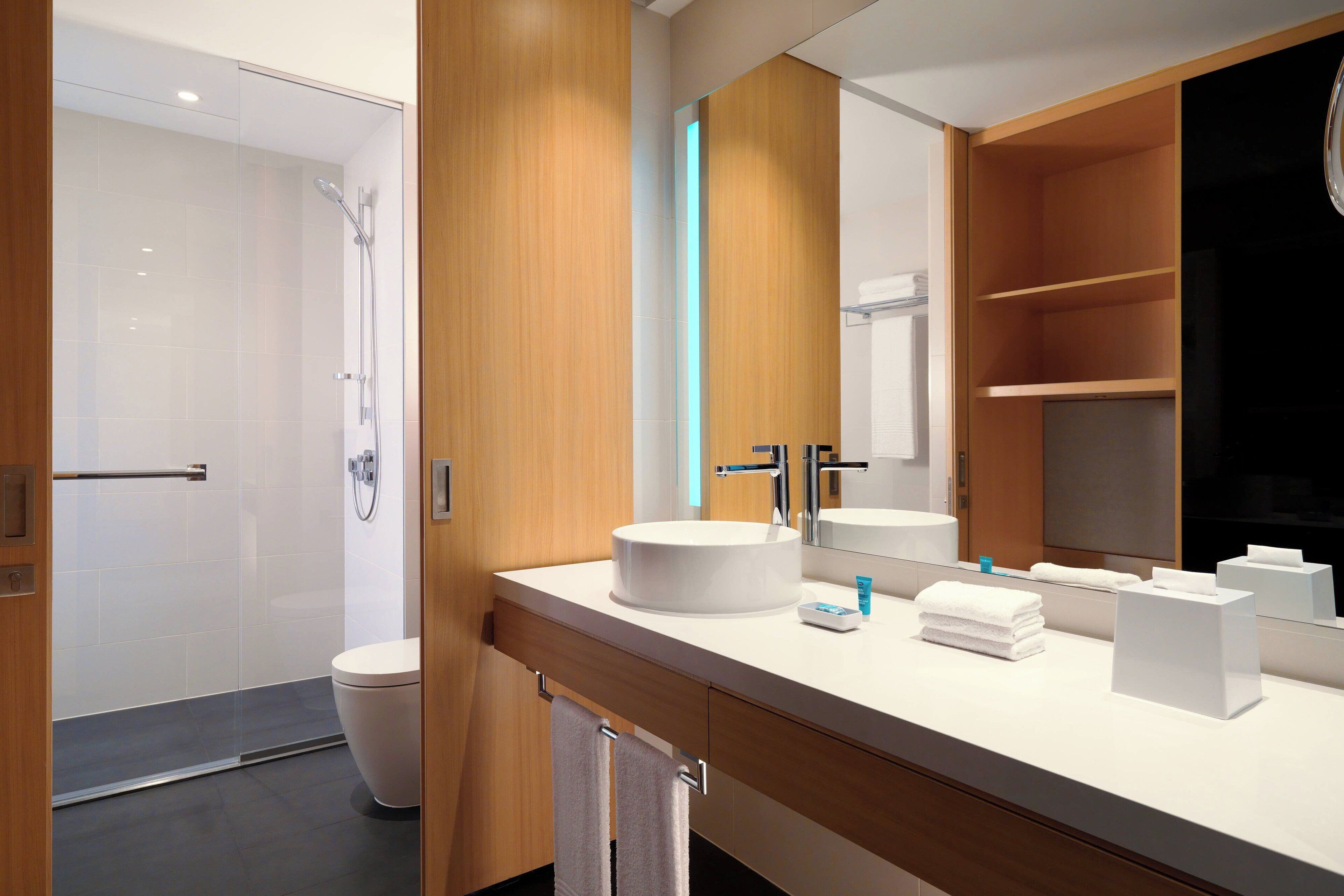 Un baño moderno con un espejo grande, un lavabo redondo y un inodoro.