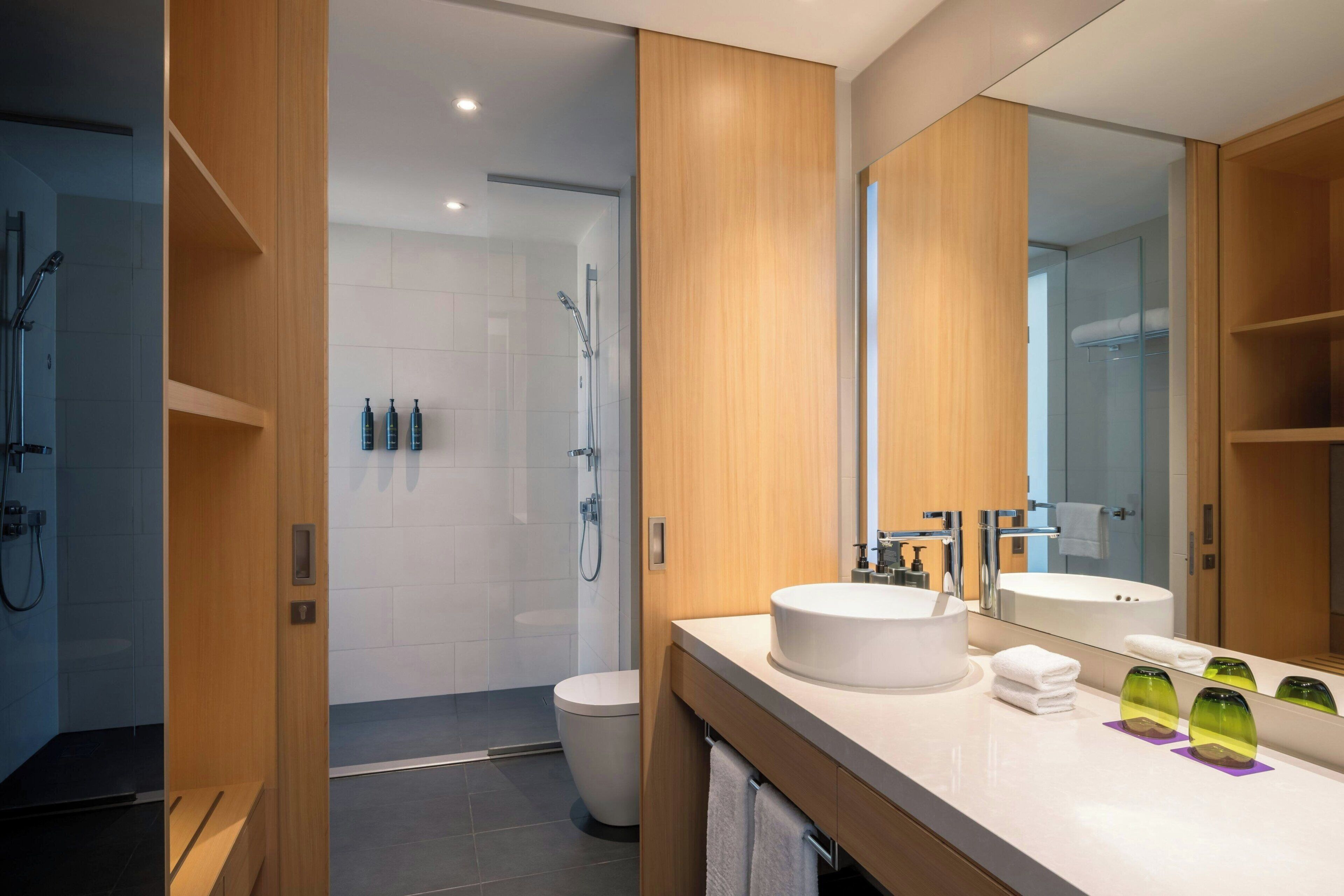 A modern bathroom with a large mirror, two sinks, and a shower area.
