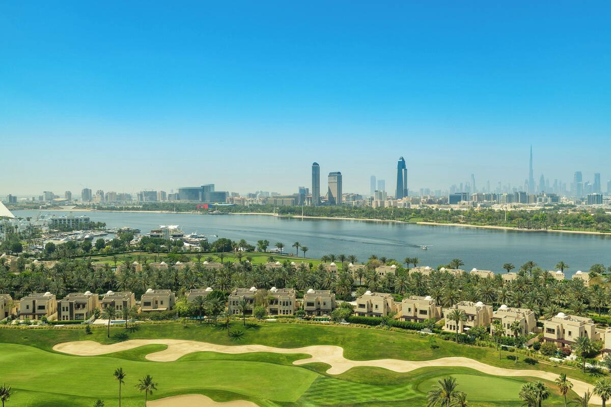 A golf course with sand bunkers and a view of a city skyline with tall buildings.