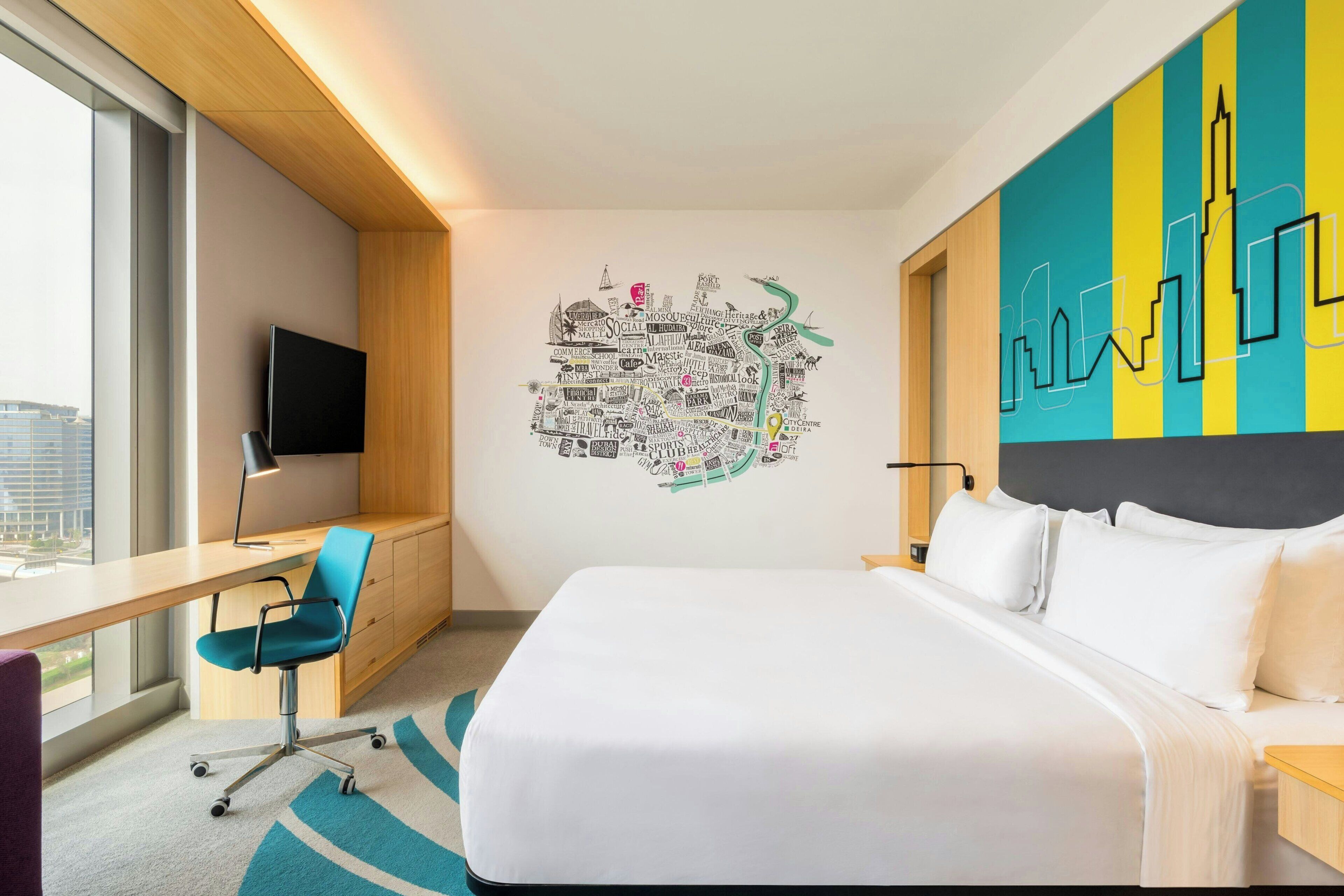 Une chambre d’hôtel avec un grand lit, un bureau avec une chaise, une télévision et une décoration murale représentant un paysage urbain.