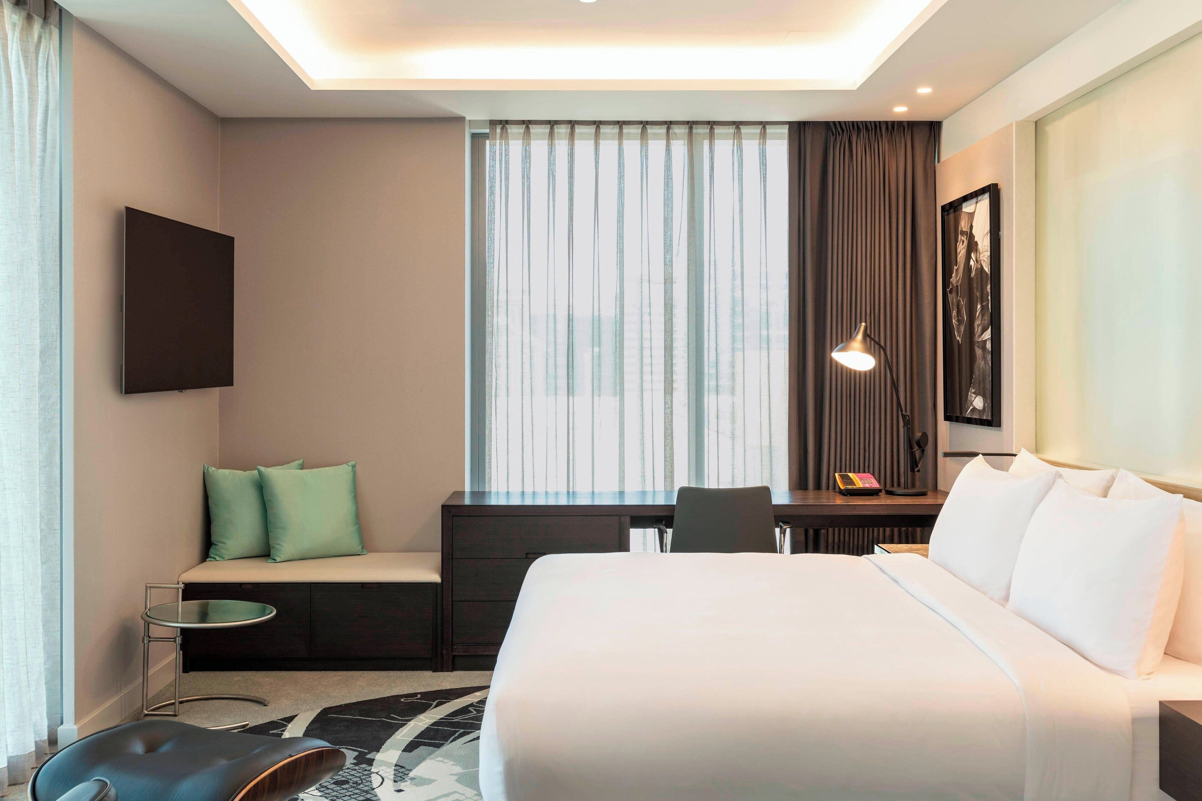 Une chambre d’hôtel moderne équipée d’un grand lit, d’un bureau, d’une chaise, d’une petite table et d’un téléviseur fixé au mur.