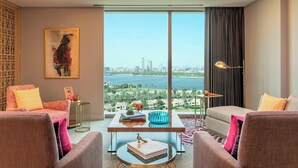 A modern living room with a large window offering a city view, a sofa, a coffee table with books and decorative items, and a floor lamp. - Aloft by Marriott Dubai Creek (Dubai)