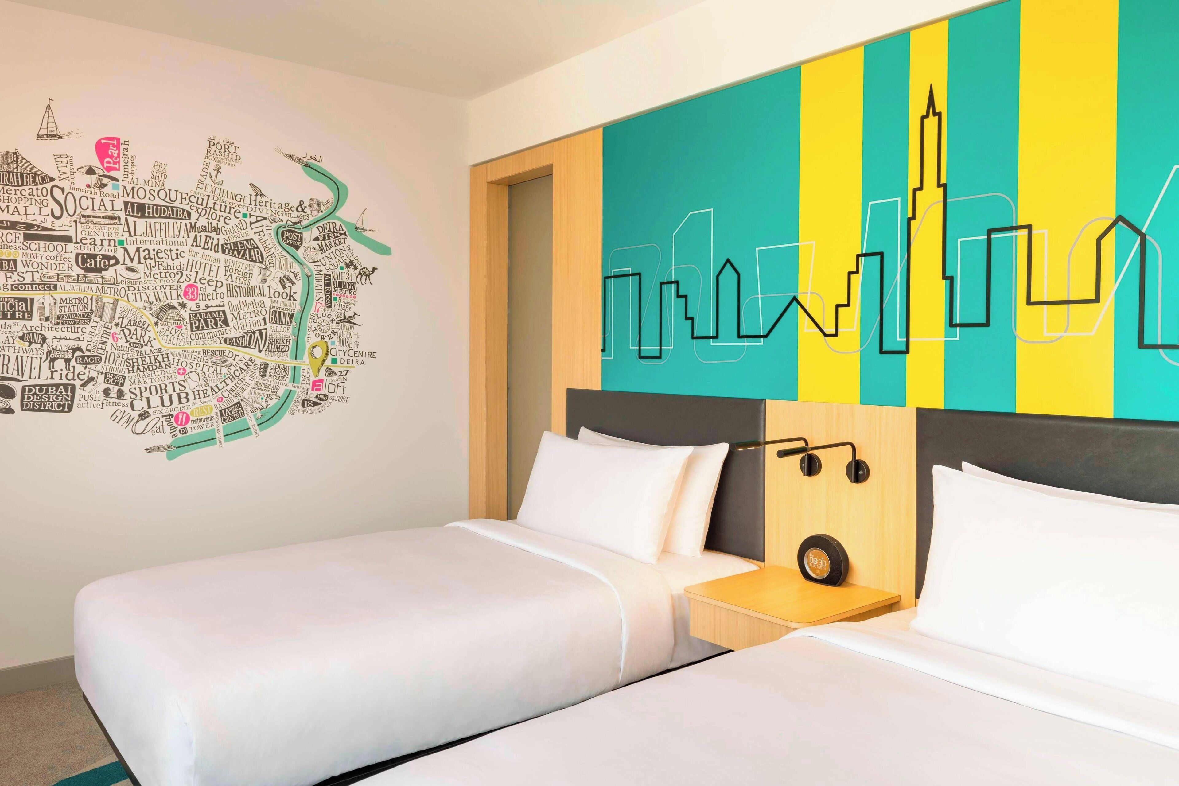 Una camera d'albergo con due letti, un quadro raffigurante un panorama urbano e un'altra opera d'arte con una mappa della città.