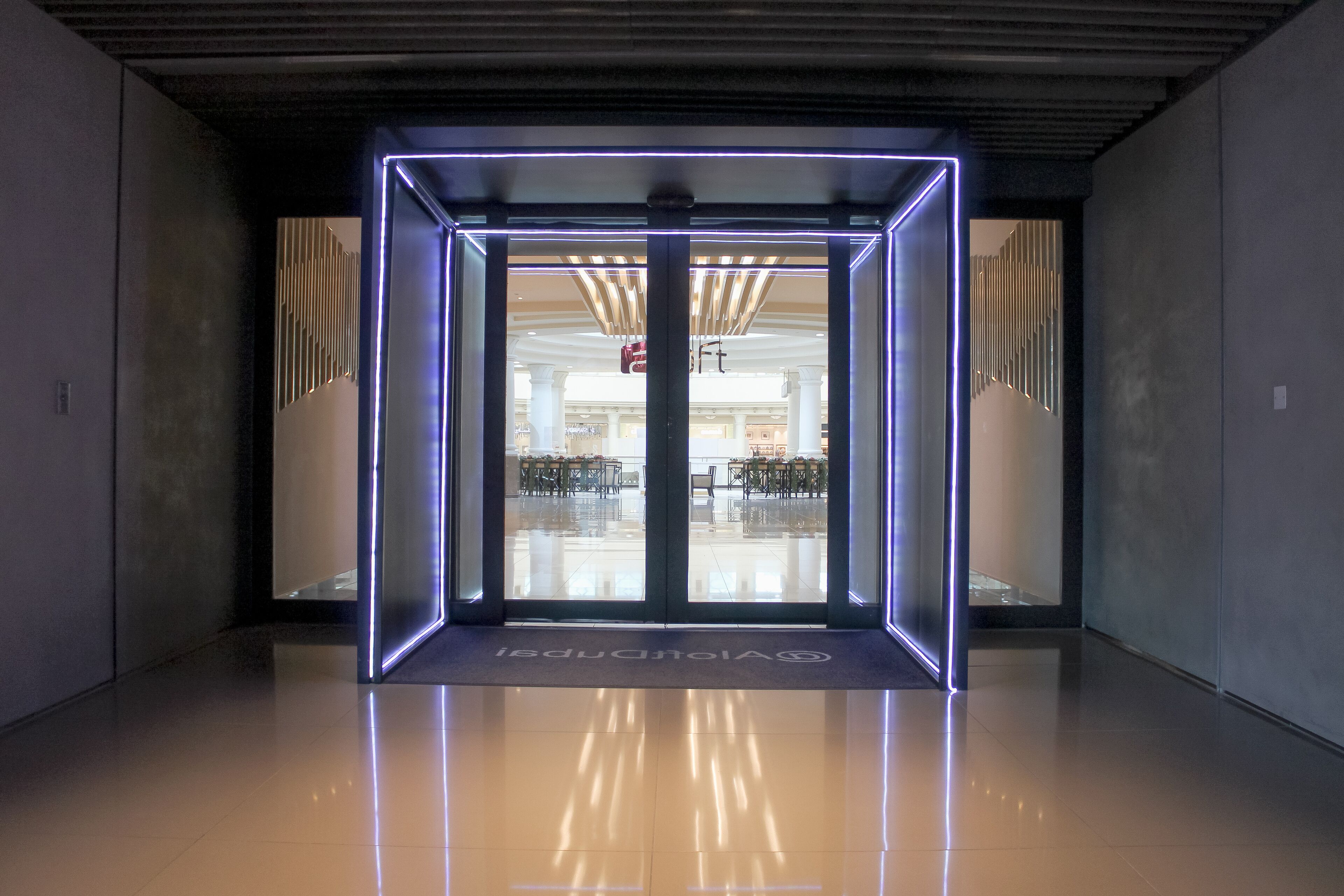 Una entrada de hotel moderna con puerta de vidrio y marco iluminado con neón.