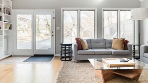 A modern living room with a grey sofa, a glass coffee table, and a bookshelf. - Oasis in the City. Morningside/VaHi. Great in town location. (Atlanta)