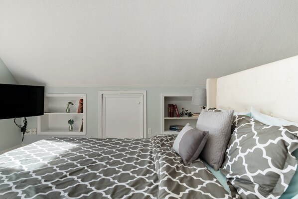 A bedroom with a bed, a television, a shelf with books and decorative items, and a door. - Oasis in the City. Morningside/VaHi. Great in town location. (Atlanta)