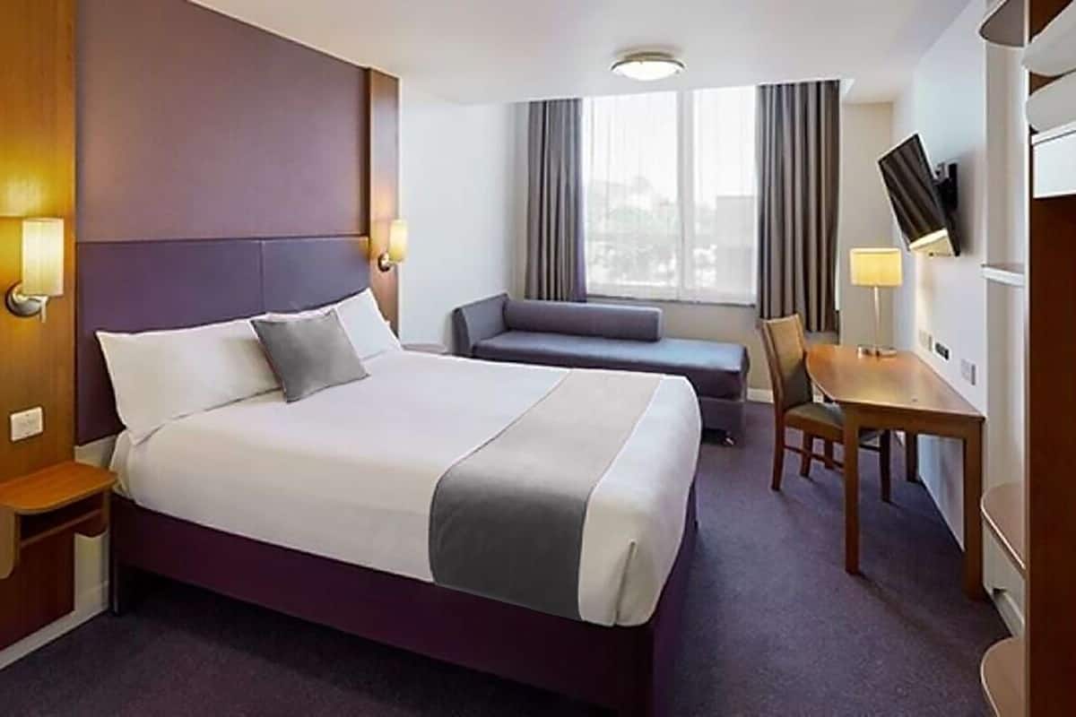 A hotel room with a large bed, a desk, a chair, and a sofa.
