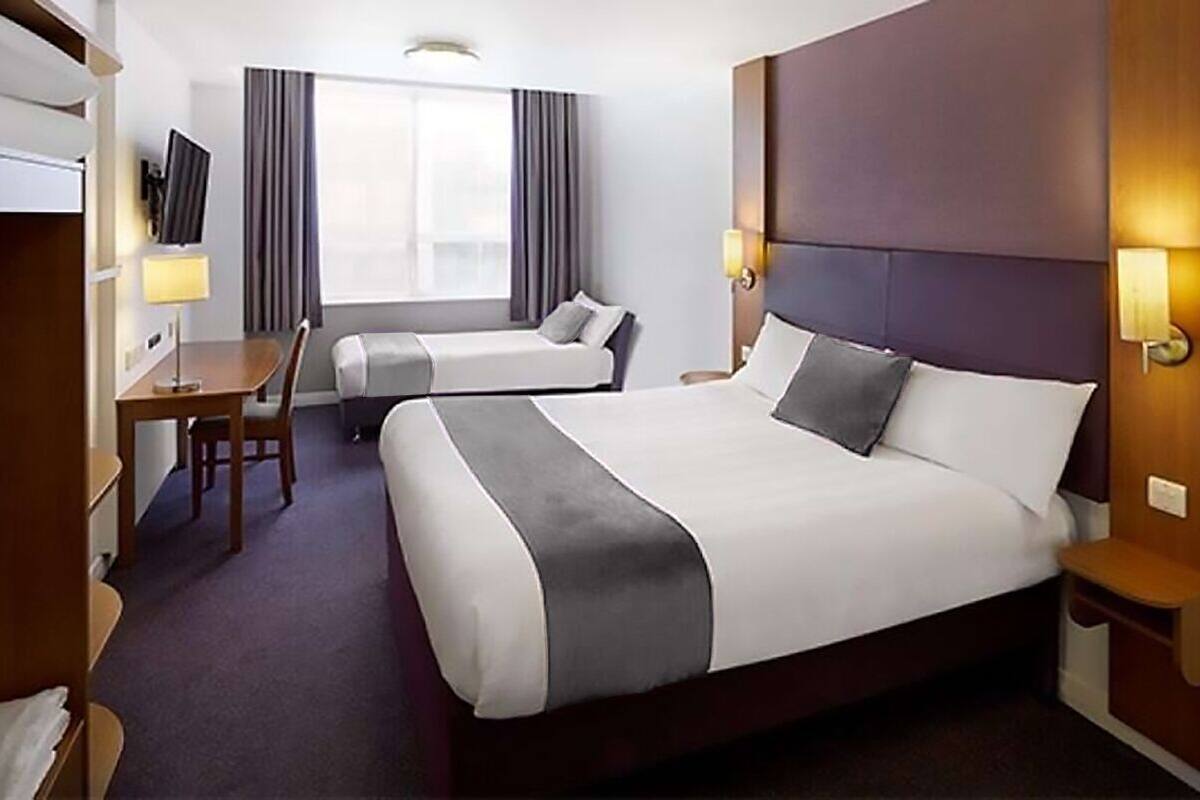 A hotel room with a large bed, a smaller bed, a desk, a chair, a TV, and a window with curtains.