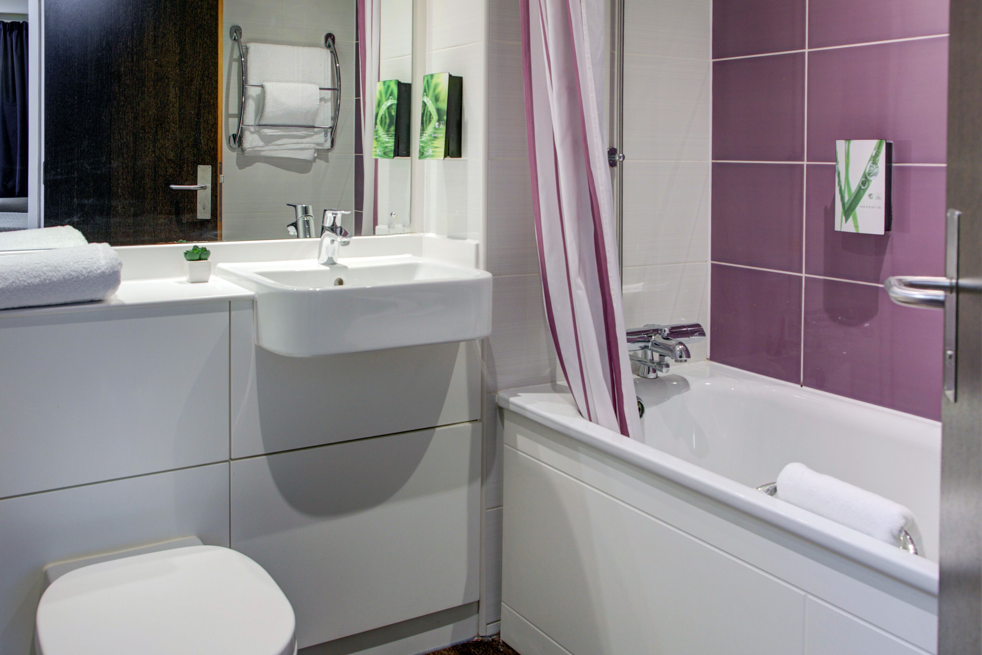 A modern bathroom with a white sink, toilet, and bathtub. There is a shower curtain and a towel rack visible.
