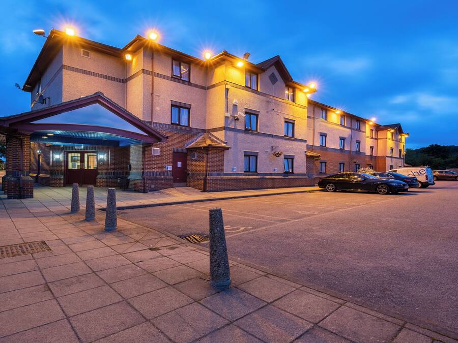 Um hotel de vários andares com fachada de tijolos, entrada coberta e área de estacionamento com carros.