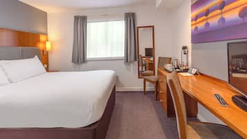 Habitación de hotel con una cama grande, un escritorio con silla, un espejo, un televisor y una ventana con cortinas.