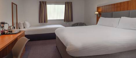 A hotel room with two beds, a desk with a coffee maker, and a window with curtains.