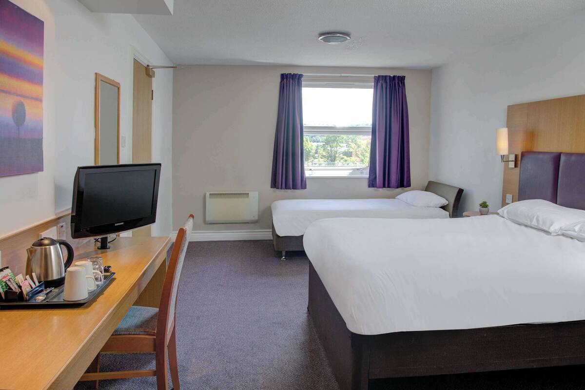 A hotel room with a desk, two beds, a television, and a window with curtains.