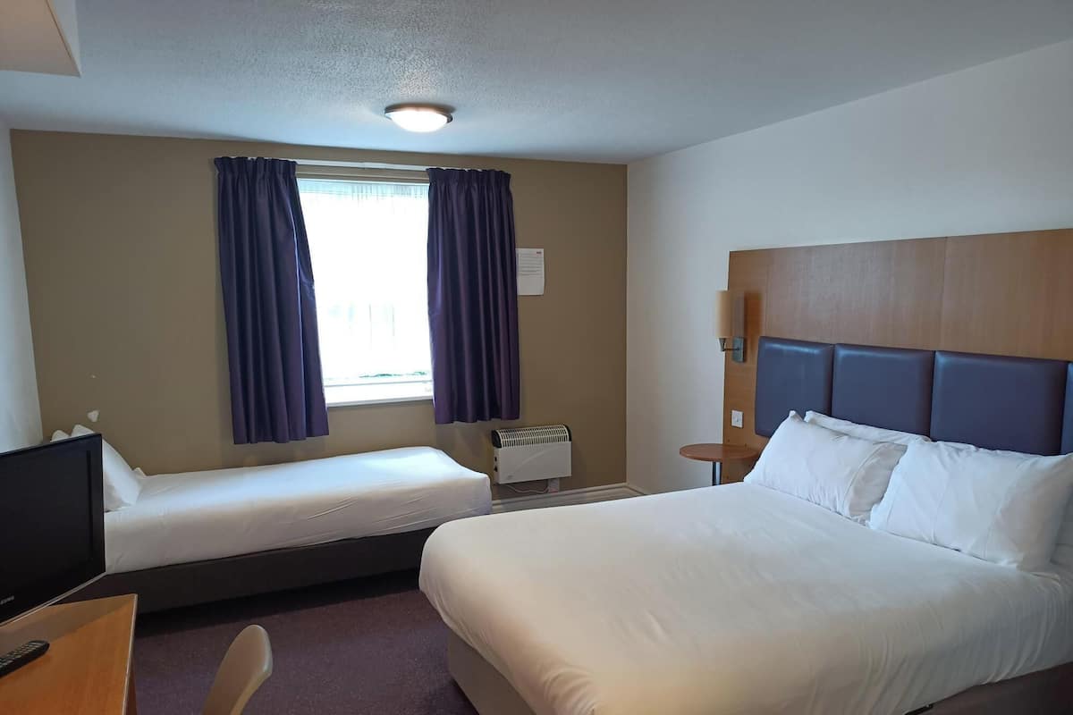 A hotel room with a large bed, a smaller bed, a desk with a TV, and a window with curtains.