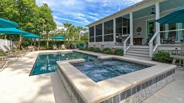 A swimming pool with a hot tub, surrounded by lounge chairs and umbrellas, and a covered patio area.