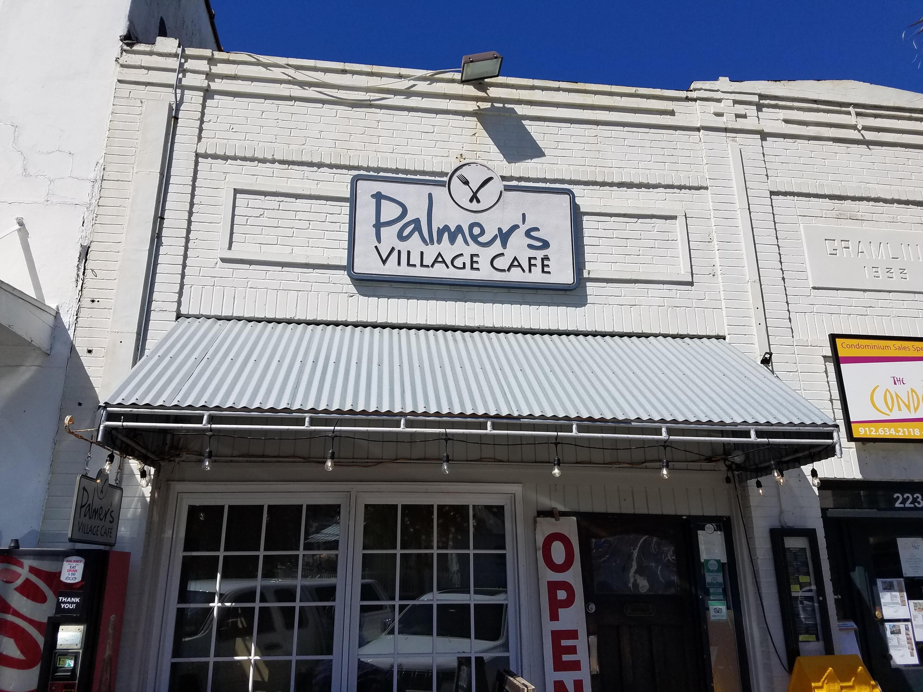Palmer's Village Cafe mit einem Schild über dem Eingang und einem ‚ÖFFNUNG‘-Schild an der Tür.