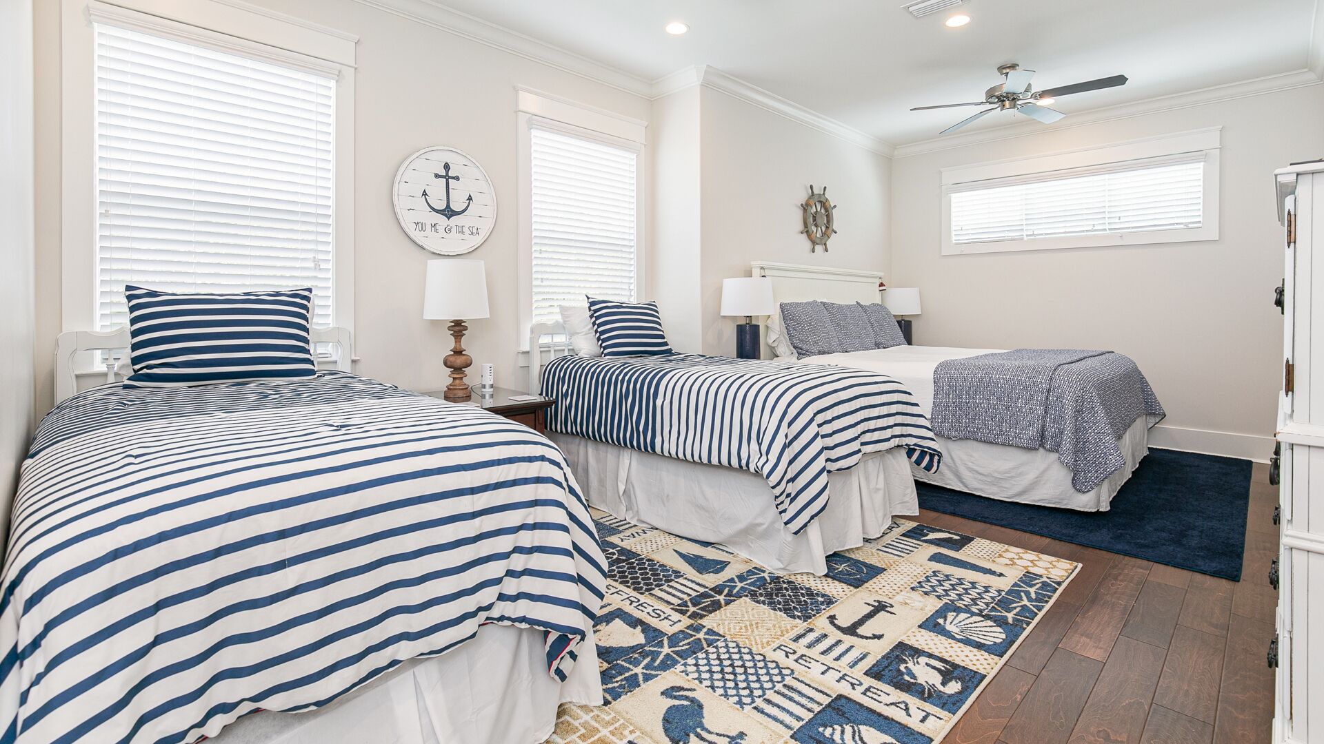 A bedroom with two beds, a ceiling fan, and nautical-themed decor.