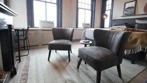 Een kamer met twee fauteuils, een bed, een bureau en grote ramen.