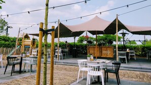Een terras met tafels en stoelen, overdekt met grote parasols, omringd door groen.