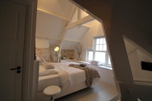 Een slaapkamer met schuine wand, een bed, nachtkastje, lamp en raam.