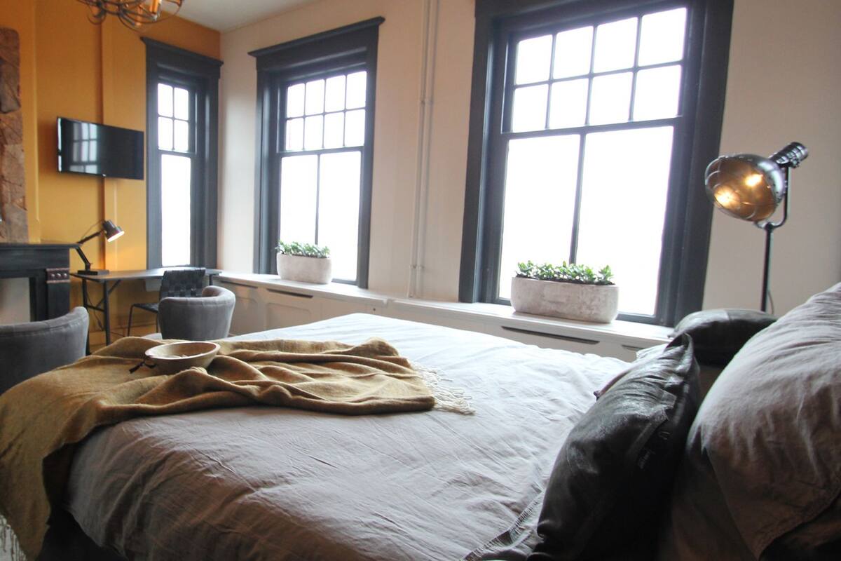 Une chambre à coucher comprenant un lit, un bureau, une chaise, un téléviseur et deux fenêtres.