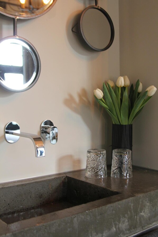 Un baño con un lavamanos, dos espejos y un florero con flores blancas.