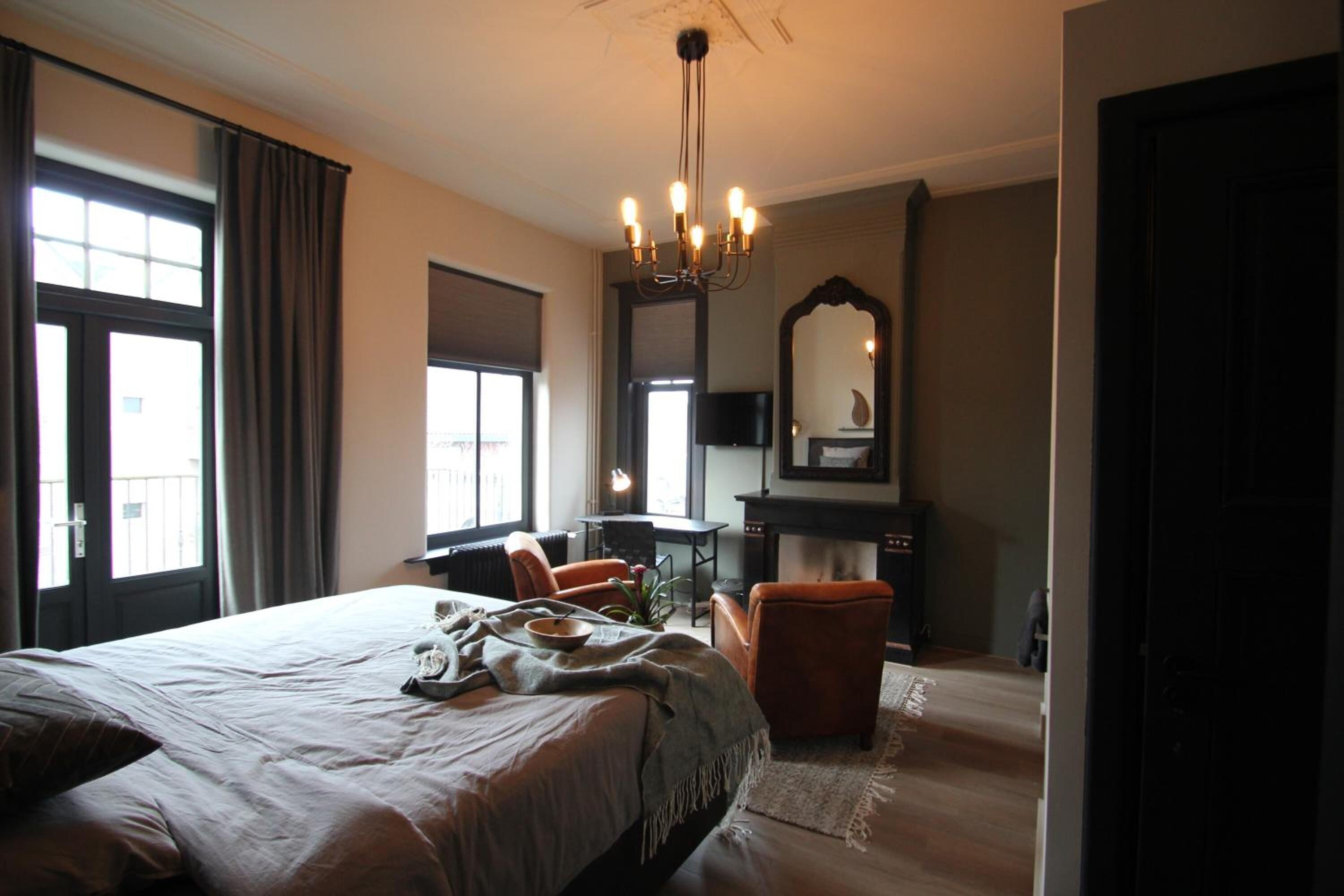 Een slaapkamer met een groot bed, een bureau, een stoel, een open haard en een spiegel.