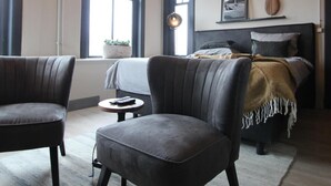 Een kamer met een bed, twee fauteuils, een tafeltje en een kroonluchter.