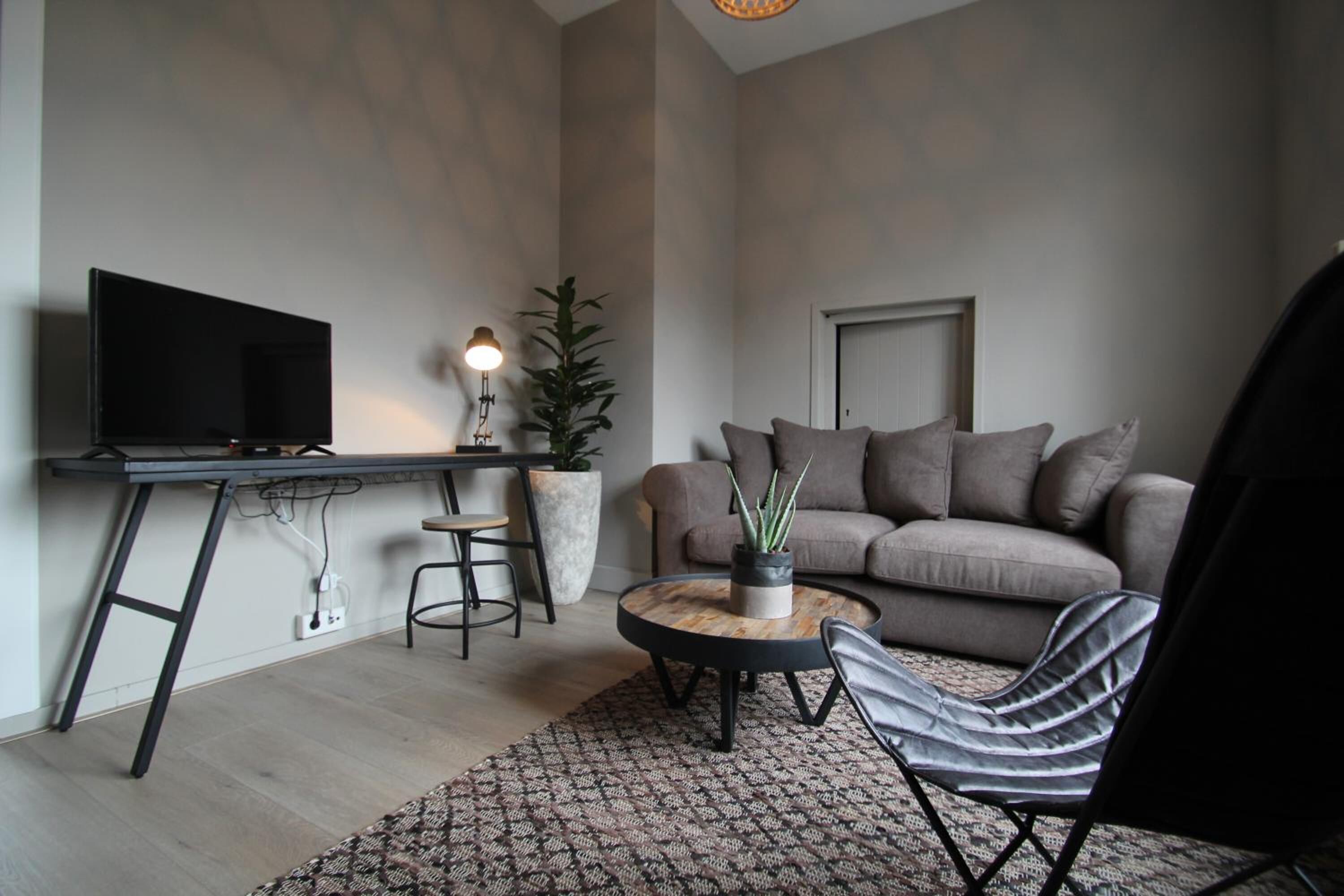 A modern living room with a flat-screen TV, a round coffee table, a sofa, and a striped chair.