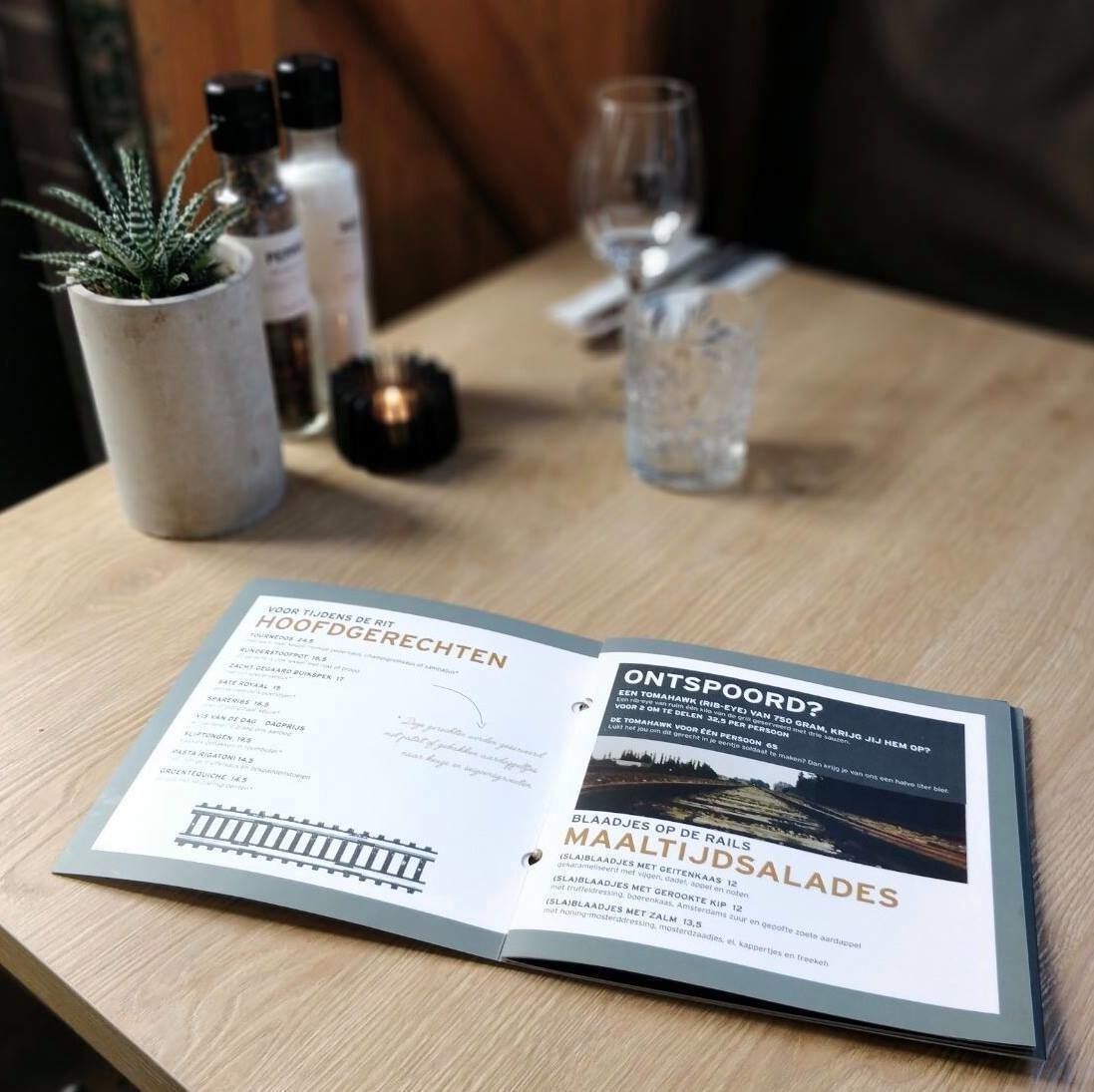 Un folleto abierto sobre una mesa de madera, con texto e imágenes relacionados con un restaurante o una experiencia gastronómica.