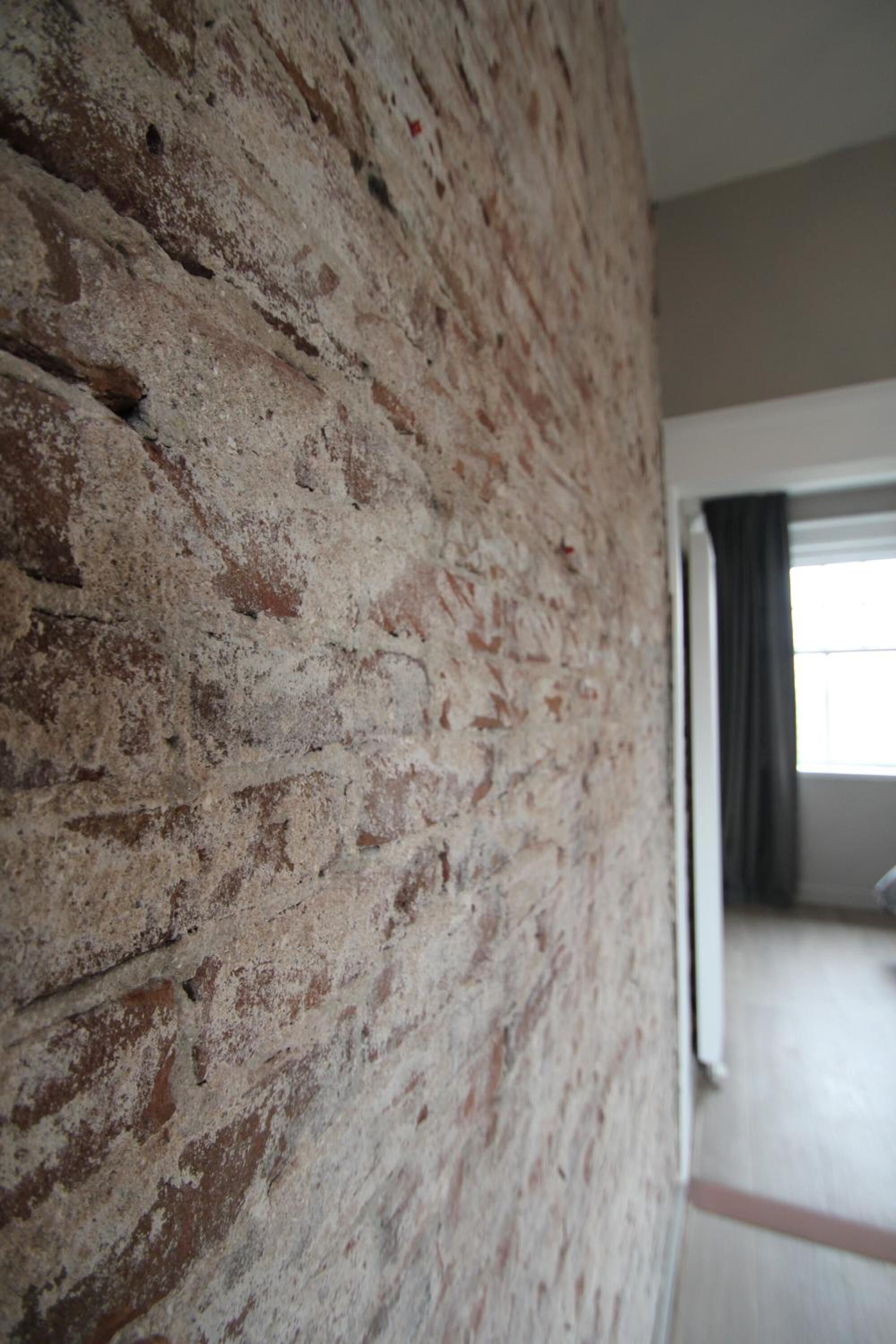 A room with a brick wall, a window with curtains, and a wooden floor.