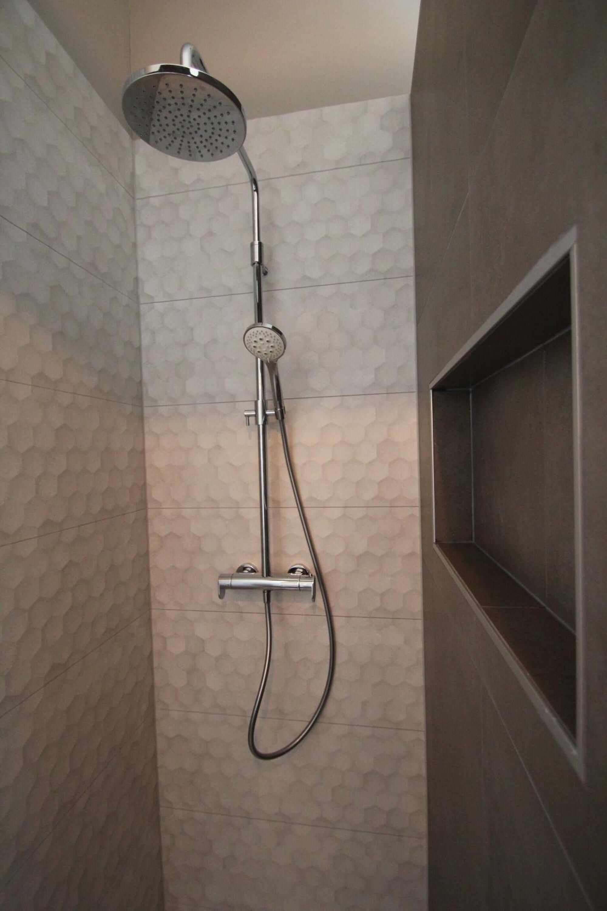 Een douche met een handdouche en een bedieningskraan aan de muur.
