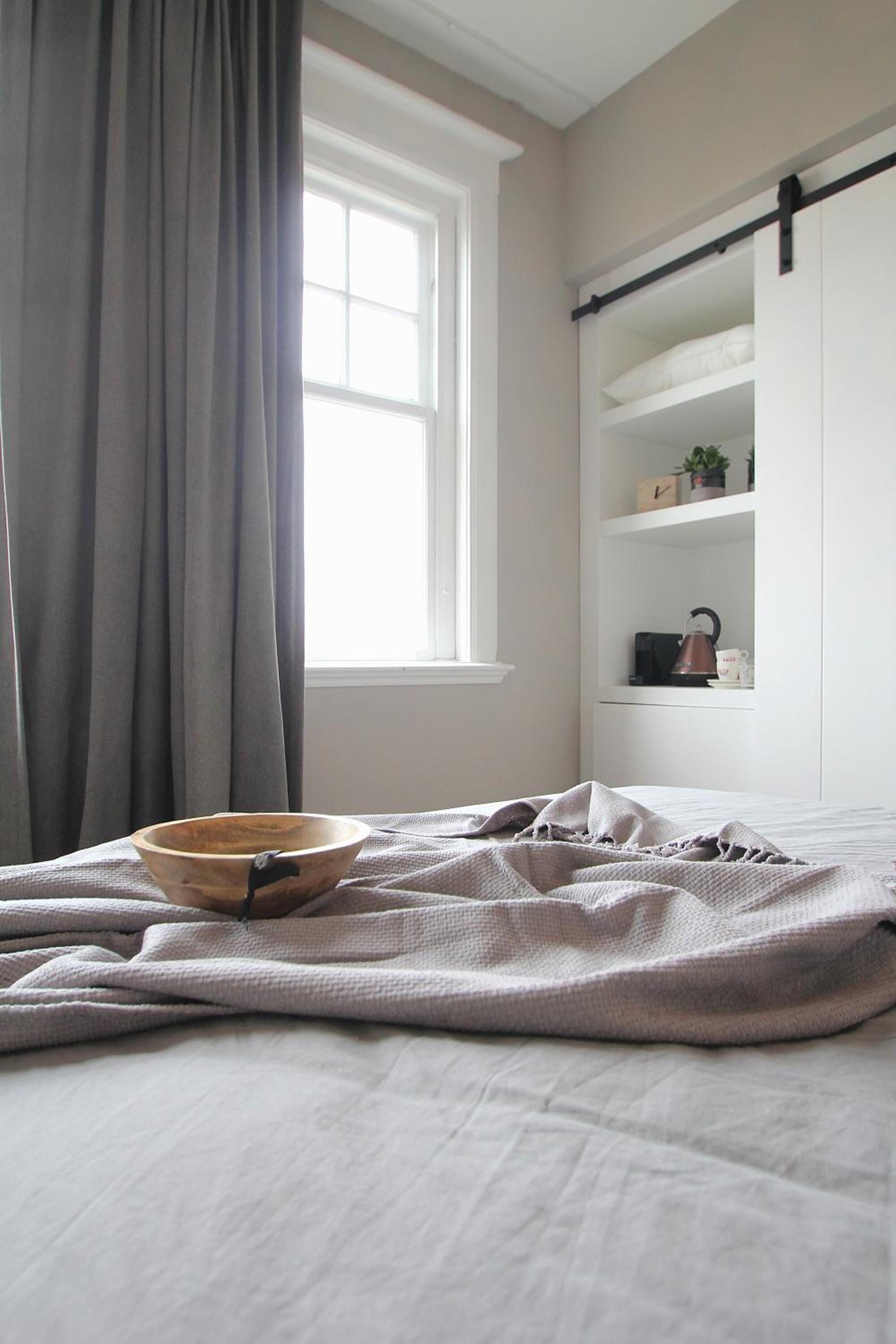 Une chambre à coucher avec un lit, une fenêtre avec des rideaux, une étagère avec des objets et un panier sur le lit.