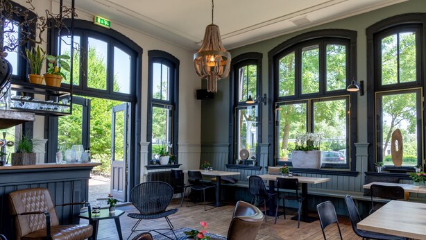 Een restaurant met hoge, gebogen ramen, houten vloeren en verschillende zithoeken, inclusief tafels en stoelen.