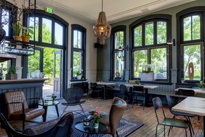 Un restaurante con amplias ventanas en arco, piso de madera y diversos tipos de asientos, incluyendo mesas y sillas.