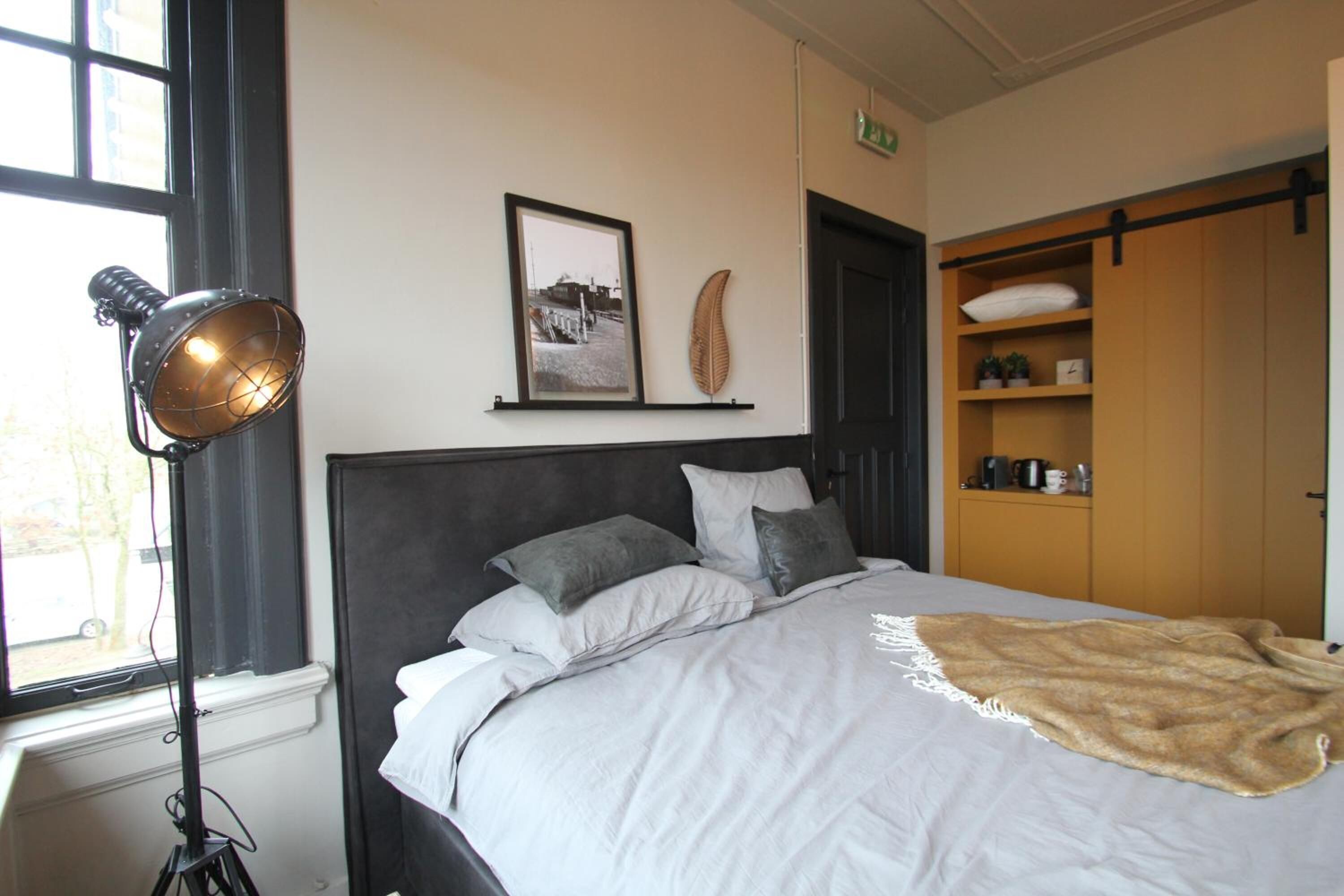 A bedroom with a bed, a floor lamp, a framed picture, and a wooden wardrobe.