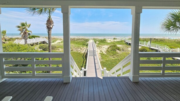 Een houten terras met uitzicht op een strand en een witte reling.