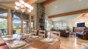 A spacious living area with a wooden dining table set for a meal, a stone fireplace, and a large television.