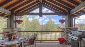 A covered outdoor patio with a stone wall, a grill, wicker furniture, and hanging flower baskets.