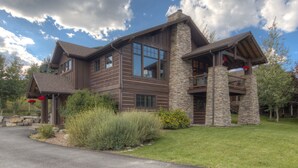 A two-story house with a stone facade and wooden siding, featuring large windows and a balcony.